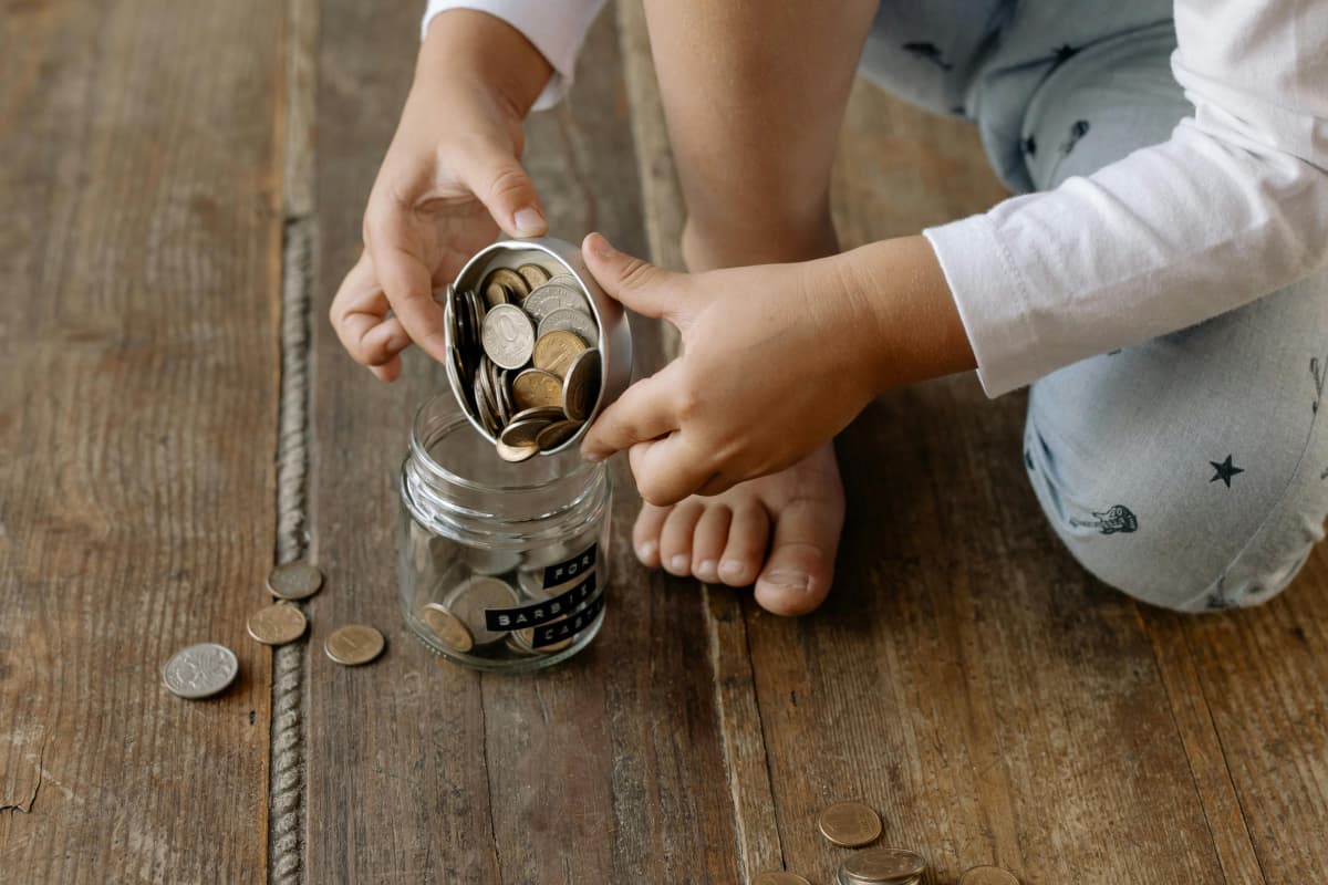 Small child emptying change out of a glass savings jar